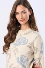 Buzo tejido en jacquard color crema con estampado de rosas azules y hojas marrones. Tiene cuello redondo y puños de rib.