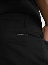 Pantalón de corte slim color negro, confeccionado en algodón y elastano, con diseño de cinco bolsillos, cierre con botón y cremallera, detalles distintivos de Calvin Klein y logo en el bolsillo trasero.