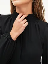 Vestido corto negro con cuello alto, mangas largas abullonadas y falda escalonada.