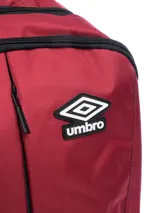 Mochila de color rojo oscuro con base y detalles en negro. Presenta el logo de Umbro en grande en vertical en el frente y el logo pequeño en el panel superior derecho. Incluye bolsillo lateral de malla.
