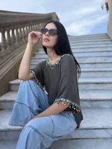 Remera tejida color gris con cuello redondo y mangas cortas. Presenta detalles de piedras de colores aplicadas en el cuello y en los bordes de las mangas.