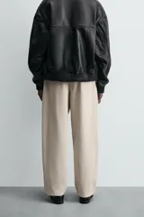 Pantalón chino color beige, de corte relaxed fit, confeccionado en tejido de mezcla de algodón y lino. Cuenta con bolsillos delanteros y traseros de vivo. Cierre frontal con cremallera y botón.