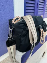 Cartera bandolera negra de nylon con detalles en charol, grifa de goma y cordones combinados. Tiene correa regulable e intercambiable.