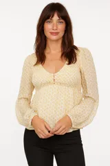 Blusa color crema con estampado floral amarillo, escote en V con botones, mangas largas abullonadas y corte a la cintura.