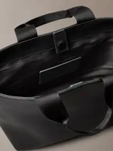 Mini cartera tote Calvin Klein negra de poliuretano con doble asa de mano y correa de hombro ajustable extraíble con el logo de la marca. Cierre con botón a presión y bolsillo interior para tarjeta.