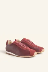 Zapatillas deportivas de cuero color borgoña con detalles en gamuza al tono, cordones finos y suela de goma blanca.