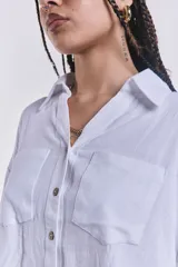 Camisa blanca de mangas cortas con dobladillo, cuello clásico, cierre frontal con botones y dos bolsillos frontales con solapa.