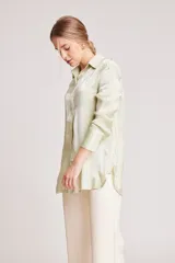 Camisa verde claro de corte recto y mangas largas con puños abotonados. Cierre frontal con botones.