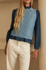 Chaleco marrón de punto con diseño trenzado, cuello redondo y sisas con volantes celestes.