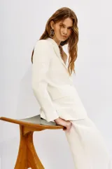 Blazer color blanco hueso, con solapas de muesca, cierre frontal con un botón y bolsillos delanteros con solapa.