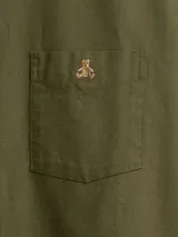 Camisa de manga larga color beige, de corte clásico, con cuello abotonado, bolsillo en el pecho y logo de oso bordado.