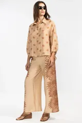 Pantalón palazzo color beige con estampado de girasoles marrones en los laterales.