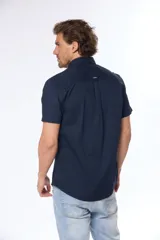 Camisa azul marino lisa de manga corta con cuello abotonado, cierre frontal con botones y bolsillo en el pecho. Confeccionada en algodón.