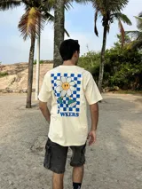 Remera beige de algodón con estampa en la espalda de una flor sonriente sobre un fondo a cuadros azules y texto "FLOWKERS".