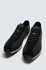 Zapatilla de cordones negra de estilo retro. Parte superior fabricada en tejido técnico y detalles en piel con acabado serraje. Suela dentada con detalle a contraste.