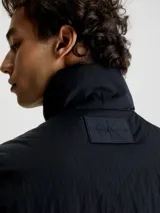 Chaleco negro acolchado de nailon reciclado con cuello alto, cierre de cremallera, bolsillos con cremallera en la cintura y logo de Calvin Klein en el pecho y la nuca.