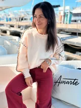 Sweater negro de tejido suave con detalles de nudos blancos en las mangas.