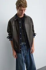 Cazadora bomber de efecto piel color marrón oscuro, con cuello solapa, cierre frontal de cremallera, bolsillos de vivo en cadera y bajo elástico.