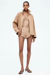 Campera color beige de sarga con cuello, cierre oculto adelante y bolsillos laterales con cierre. Modelo de corte holgado con pinzas en los codos para dar forma y cordón para ajustar elástico con topes en el bajo. Sin forrar.