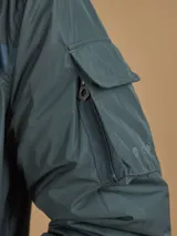 Abrigo largo color gris oscuro con capucha y forro naranja, cuenta con múltiples bolsillos.