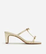 Sandalia mule dorada con punta cuadrada, tiras finas con detalle de lazos y tacón cuadrado mediano.