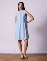 Vestido blanco de algodón y rayón, marca Dash. Cuello a la base, sin mangas y abertura central con botones. Delantera con detalle plisado y laterales con bolsillos.