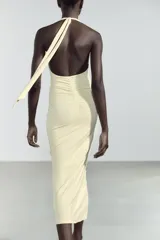 Vestido largo color amarillo pálido, con cuello halter que se ata en la nuca, escote en pico y frunces laterales.