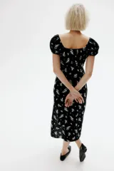Vestido largo negro con estampado floral blanco, de tejido liviano de mezcla de lino y viscosa. Modelo con mangas cortas abullonadas, escote corazón con tiras finas y copas preformadas con frunces. Elástico fino en escote, hombros, mangas y cintura. Cierre lateral oculta y bajo recto con tajo pronunciado en un lado.