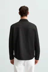 Sobrecamisa negra de tejido con elasticidad, cuello solapa, manga larga con puño abotonado, bolsillos de plastrón en el pecho y cierre frontal con botones a presión.