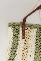 Bolso tipo tote de rafia tejida a rayas horizontales en tonos beige y marrón, con asas de cuero marrón.