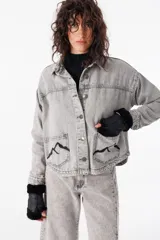 Camisa corta de jean gris con terminación redondeada en el ruedo. Presenta dos bolsillos plaqué bordados con motivo de montaña y detalle de pespunte a contratono.