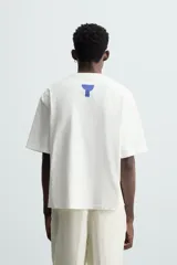 Camiseta blanca de corte regular, cuello redondo y manga corta. Presenta parches geométricos en azul, negro y rojo en el frente y estampado en la espalda.