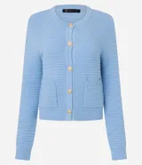 Cardigan de punto blanco, con cuello redondo, manga larga y cierre frontal de botones dorados. Posee dos bolsillos cuadrados en la parte delantera inferior.