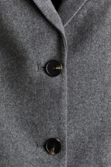 Blazer gris de corte entallado, con solapas de muesca, botonadura sencilla, bolsillo superior insertado y bolsillos delanteros. Tiene hombreras, botón decorativo en los puños y abertura atrás.