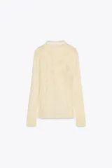 Blusa color crema de viscosa con cuello redondo y manga larga abullonada. Detalle de bordados con aplicación de abalorios y cierre frontal con botones.