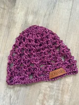 Gorro de hilo color lila, tejido a crochet con diseño calado y etiqueta de cuero con la marca.