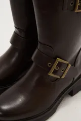 Bota corta de estilo motociclista color negro, con caña media y suela track gruesa. Presenta dos correas ajustables con hebillas metálicas plateadas alrededor del tobillo y la caña.