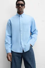 Camisa celeste de lyocell y algodón, corte relaxed fit, cuello solapa, manga larga con puños abotonados, bolsillo de parche en el pecho y cierre frontal con botones.