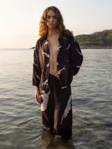 Camisa negra con estampado de figuras humanas blancas, cuello clásico, cierre frontal con botones y mangas 3/4 con lazos ajustables en los puños.