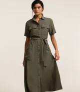 Vestido midi color verde militar, estilo camisero, con cuello clásico, mangas cortas, abotonadura frontal completa, bolsillos utilitarios en el pecho, lazo en la cintura y falda acampanada.