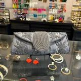 Sobre de fiesta color beige, bordado con mostacillas doradas formando motivos florales. Tiene cierre con solapa y asa de cadena dorada para llevar al hombro.