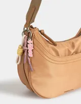 Bandolera hobo negra de tela deportiva con correa regulable, cierre superior, bolsillo frontal y charm lateral decorativo.