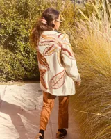 Cárdigan de lana color crudo con apliques de hojas bordadas en tonos marrones, naranjas y amarillos. Corte holgado y largo a la cadera.