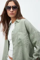 Camisa verde seco de lino, de corte holgado, con cuello clásico, cierre frontal con botones, manga larga y bolsillo de parche en el pecho.