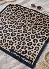Pañuelo cuadrado de poliéster con estampado de leopardo en tonos beige, marrón y negro. Presenta un borde liso de color azul marino con el nombre "VIVIANA MÉNDEZ" impreso en blanco.