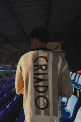 Sweater de punto a rayas verticales azules y blancas, con cuello polo negro y logo bordado en el pecho.