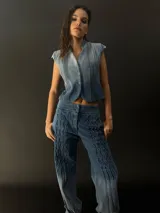 Chaleco de denim azul con cuello y pequeñas mangas, diseñado con alforzas laterales.