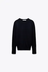 Sweater negro de punto liso con cuello redondo y mangas largas con botones dorados en los puños.