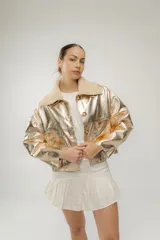 Campera corta dorada de cuero sintético metalizado con cuello de piel sintética color crema, cierre frontal con botones marrones y bolsillos de parche en el pecho.