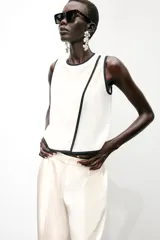 Blusa blanca sin mangas de crepe con cuello redondo y detalle de ribete negro en cuello, sisas y abertura frontal diagonal.